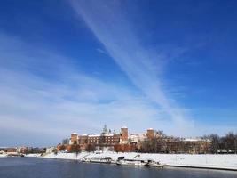 panorama del castillo real de wawel ubicado en la margen izquierda del río vistula en la ciudad de cracovia, polonia. soleado día de invierno, gran cielo azul, líneas de nubes blancas. lugar para el texto. foto