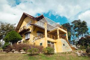 View on a yellow house with garden on a background of trees and cloudy blue sky. photo
