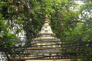 View on a Buddhist temple between trees with electric wires on a foreground. Chiang Mai, Thailand. photo