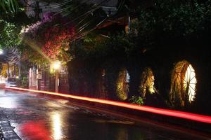 vista en una calle nocturna de la ciudad con linterna y transporte en movimiento en un clima lluvioso. larga exposición. Chiang Mai, Tailandia. foto