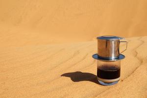 goteo de café negro al estilo vietnamita con leche condensada en una arena roja con espacio para copiar. método tradicional de hacer café. desayuno en un desierto. foto