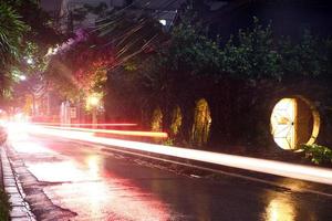 View on a night street of city with lantern and moving transport in a rainy weather. Long exposure. Chiang Mai, Thailand. photo