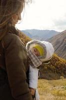 retrato de una joven hermosa mujer con su pequeña hija dormida en un portabebés ergo sobre un fondo de montañas otoñales. montañas del cáucaso, georgia. foto