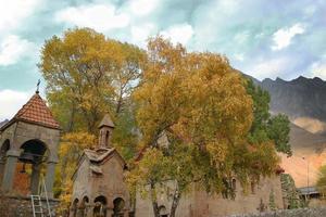 View on Medieval Orthodox Church with autumn trees on a background of mountains in cloudy weather. Caucasus Mountains, Georgia. photo
