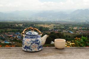 Chinese teapot and cup with green tea on a wooden table on a background of scenic mountains landscape. Pai, Thailand. photo