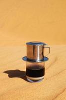 Drip Black Coffee in Vietnamese style with condensed milk on a red sand. Traditional method of making coffee. photo