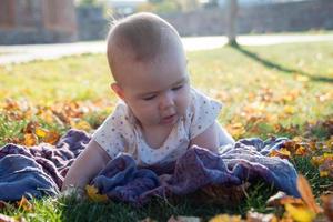 Cute little girl is lying on a grass and playing with dry yellow leaves. photo