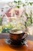 Cup with hot milk coffee on a colorful wooden table in a cafe on background of city view. Dalat, Vietnam. photo