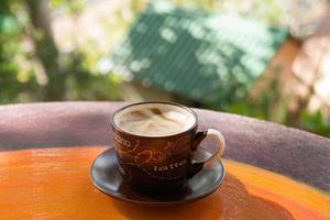 Cup with hot milk coffee on a colorful table in a cafe on background of city view. Dalat, Vietnam. photo