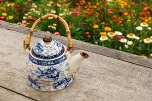 Chinese teapot with green tea on a wooden table on a background of bright colorful flowers, top view. Pai, Thailand. photo