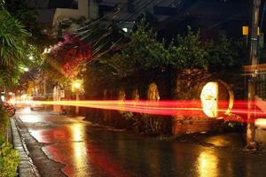 vista en una calle nocturna de la ciudad con linterna y transporte en movimiento en un clima lluvioso. larga exposición. Chiang Mai, Tailandia. foto