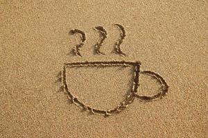 una taza de café se dibuja en una playa de arena en una puesta de sol, vista superior. foto