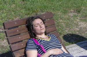 una joven morena yace en una chaise longue de madera en un parque de la ciudad en un día soleado foto