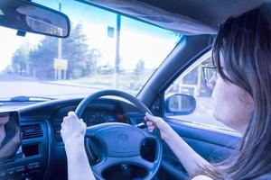 a brunette woman with glasses is driving a car with a right hand drive photo