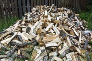 a pile of chopped birch wood is poured out on the grass in front of the fence, stove heating, fuel for fireplaces, stoves photo