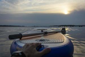 sup board, paddle board con un remo a la luz del atardecer en el fondo del primer plano del agua. equipo de embarque sup. foto