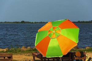 A beach umbrella from the sun and a wooden chaise longue on the beach, sunlight, water and sand. photo