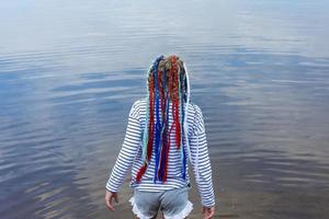 A teenage girl with bright multicolored ribbons braided in pigtails, a modern youth hairstyle, a girl goes into the water of the lake photo