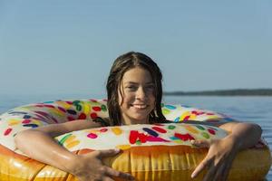 Cute teen girl with colorful inflatable swimming circle swims in the blue water of the sea on a hot sunny day photo