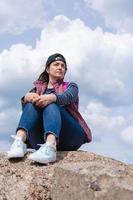 A young beautiful woman in a baseball cap sits on the rocks by the sea and looks into the distance. photo