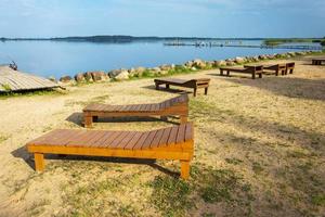 A row of wooden sun beds on the beach. Sunlight, water and sand. The beach on the lake of the tourist base. photo