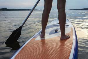 una niña nada en una tabla de sup, hermosas piernas femeninas en una tabla de sup con un remo en un hermoso lago foto