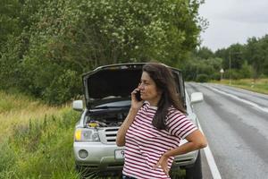 A broken car. A young woman stands on the road by a broken car. A phone call to help with a broken car. photo