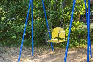 children's swing on the playground in the yard in summer among the greenery photo