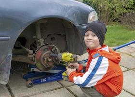 The boy is a car mechanic. The son helps his father to change winter wheels for summer ones. Car repair, children's mechanic worker. photo