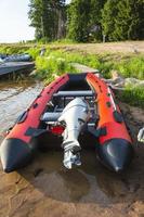 Red inflatable rubber boat with a motor near the lake shore, fishing, tourism, active recreation photo