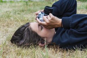 Cute teen girl with a camera, a girl taking pictures on a retro vintage camera on the grass in the park, a hobby concept photo