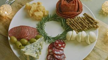 charcutería plana con salami, diferentes tipos de queso. tiene frutos secos, frutos secos varios y miel. arreglo de vacaciones con velas encendidas video