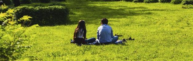 Young couple sitting with their back to the camera on the grass in the park, happy couple relaxing on the grass photo