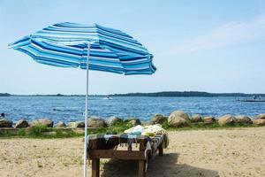 A beach umbrella from the sun and a wooden chaise longue on the beach, sunlight, water and sand. photo