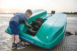 un niño repara un bote en la orilla de una bahía marina, un viejo catamarán, una hélice, un niño mecánico foto