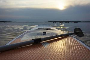 SUP board, Paddle board with a paddle in the sunset light on the background of water close-up. SUP boarding equipment. photo