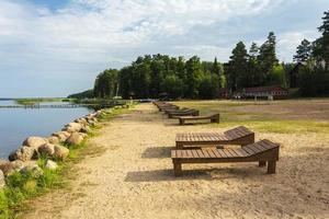 A row of wooden sun beds on the beach. Sunlight, water and sand. The beach on the lake of the tourist base. photo