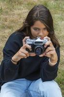 Cute teen girl with a camera, a girl taking pictures on a retro vintage camera on the grass in the park, a hobby concept photo