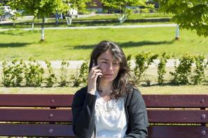 linda chica caucásica con un teléfono en un banco del parque en verano foto