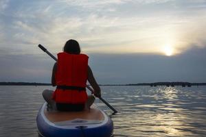 una adolescente nada en una tabla de sup, una hermosa niña monta una tabla con un remo en un hermoso lago, río foto