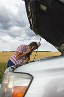 A broken car. A young woman stands on the road by a broken car. A phone call to help with a broken car. photo