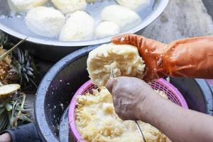 A woman's hand held a fork to grate the pineapple into small pieces to prepare to be processed into a stirring pineapple. photo