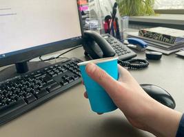 taza de café azul de cartón de una cafetería en un escritorio con una computadora con teclado y mouse y suministros de oficina de un trabajador de oficina durante el almuerzo. pausa para el café de negocios foto