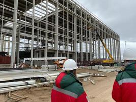 Back view portrait of two construction workers wearing hardhats and reflective vests discussing engineering plans on site, copy space photo