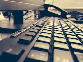 Close-up view of a black plastic keyboard with buttons on a working computer with a monitor and a telephone in a business office photo