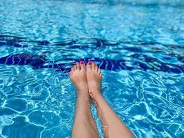 pies en el agua de la piscina. selfie de piernas y pies descalzos con pedicura roja y uñas de manicura sobre fondo azul del mar. vacaciones en vacaciones de verano foto