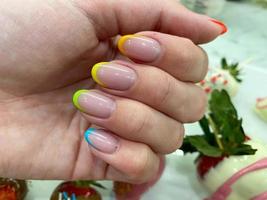 Hermosa manicura de mujer multicolor a la moda con estilo francés en los dedos con barniz de gel de diferentes colores del arco iris transparente amarillo rojo verde azul. diseño de uñas con estilo foto