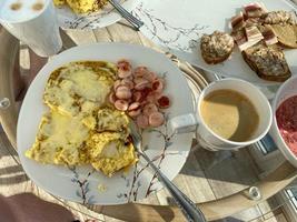 Breakfast is served on a light board. Fried eggs, omelet, croissant, coffee, dessert, place for text. In the hands of a fork and a cup of coffee photo