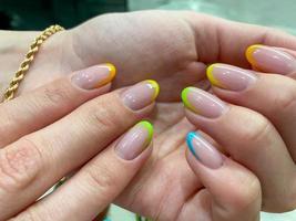 manicura multicolor colorida en uñas cortas sobre fondo amarillo. arte de uñas. esmalte de uñas rosa, verde, amarillo, melocotón foto