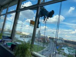 un trabajador de limpieza de ventanas, un escalador industrial cuelga de un edificio alto, un rascacielos y lava grandes ventanas de vidrio para limpiarlas en lo alto de una gran ciudad en un edificio de oficinas foto